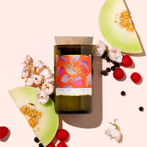 Mojo Candle Co. Australiana Reclaimed Wine Bottle Soy Wax Candle Kakadu Plum lifestyle shot with melon slices, peppercorns and flowers on peach