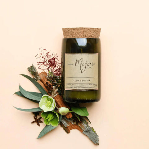 Mojo Candle Co. Wine Bottle Soy Wax Candle Cedar & Saffron lifestyle shot of the bottle candle among cinnamon sticks, star anise and leaves on peach