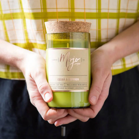 Mojo Candle Co. Wine Bottle Soy Wax Candle Cedar & Saffron lifestyle shot of two hands holding the corked bottle candle in front of a checked shirt