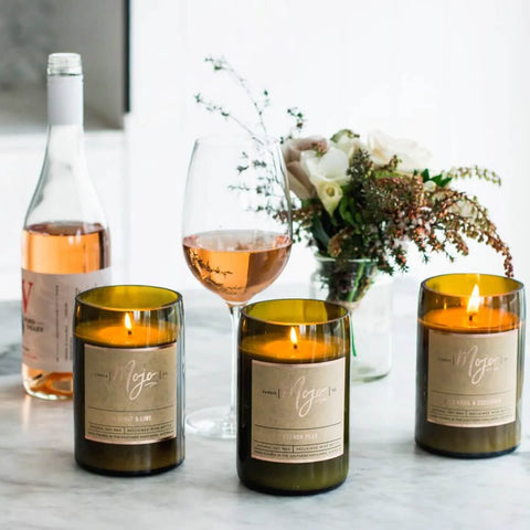 Mojo Candle Co. Wine Bottle Soy Wax Candle Oakmoss & Sage lifestyle shot of three lit bottle candles beside glasses of rosé and a vase of flowers