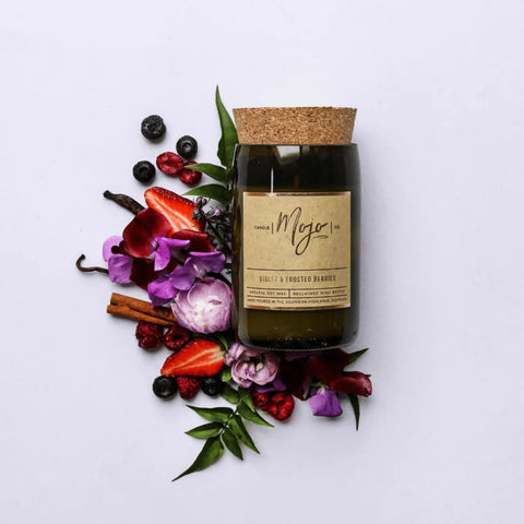 Mojo Candle Co. Wine Bottle Soy Wax Candle Violet & Frosted Berries lifestyle shot of the bottle candle among berries and flowers on a lilac backdrop
