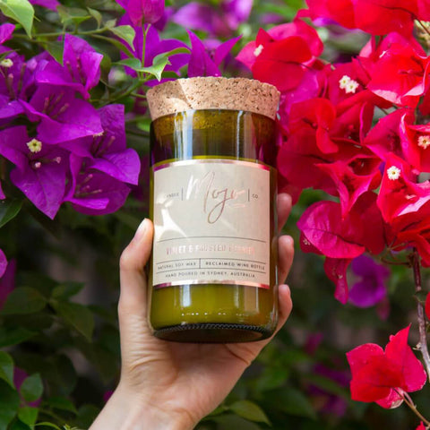 Mojo Candle Co. Wine Bottle Soy Wax Candle Violet & Frosted Berries lifestyle shot of a hand holding the bottle candle among pink bougainvillea