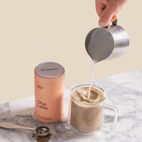 Morning Made Chai Latte Original Blend 300g lifestyle shot of milk being poured into a glass mug beside the peach tin on a marble bench