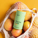 Morning Made Matcha Latte Mango Blend 300g lifestyle shot of the green tin in a mesh bag of ripe mangoes on a yellow backdrop
