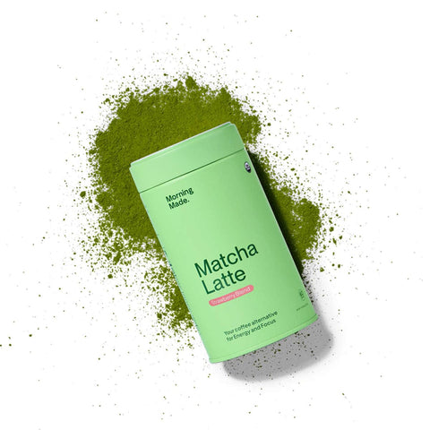 Morning Made Matcha Latte Strawberry Blend lifestyle shot of the tin lying in a spill of green matcha powder on a plain white background