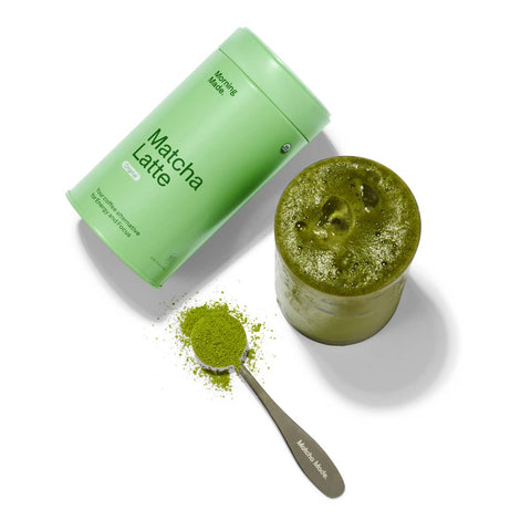 Morning Made Matcha Latte Sweetened Blend 300g lifestyle flat lay of the tin beside an open pot of matcha and a spoon of powder on white