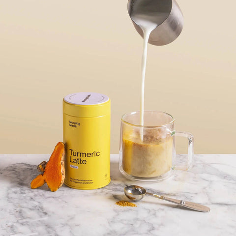 Morning Made Turmeric Latte Original Blend 300g lifestyle shot of milk being poured into a glass mug beside the yellow tin and orange turmeric