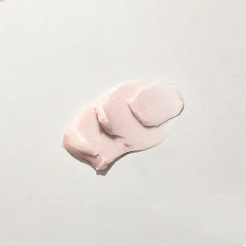 A dollop of pale pink cream or lotion on a plain light background.