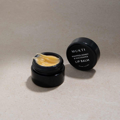 Black lip balm container with open lid showing yellowish balm on a beige background.