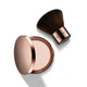 Nude By Nature Kabuki Brush 07 with a dark bristle head beside an open compact of pressed powder on a plain white background, clear product photo