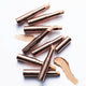 Nude By Nature Perfecting Concealer group shot of several rose gold topped concealer wands lying on white beside a smear of concealer, overhead