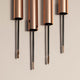 Four rose gold mascara tubes with black threads on a beige background.