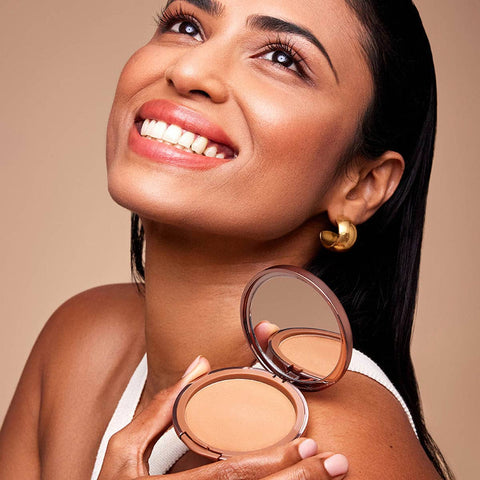 Woman holding a compact powder with a beige background.