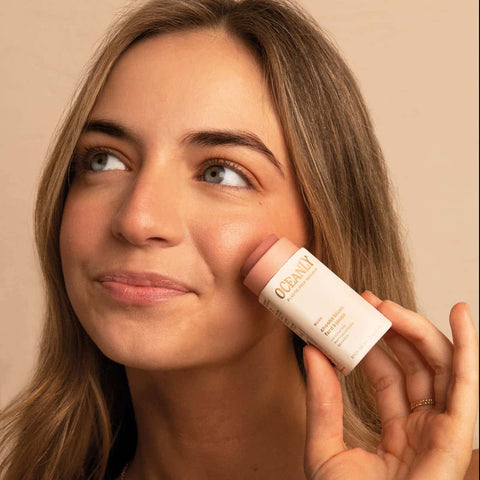 Model applying rose blush stick to her cheek. 