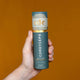 Hand holding tube of Cordyceps Mushroom Honey Pearls against an orange background. 