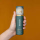 Hand holding tube of Reishi Mushroom Honey Pearls against an orange background. 