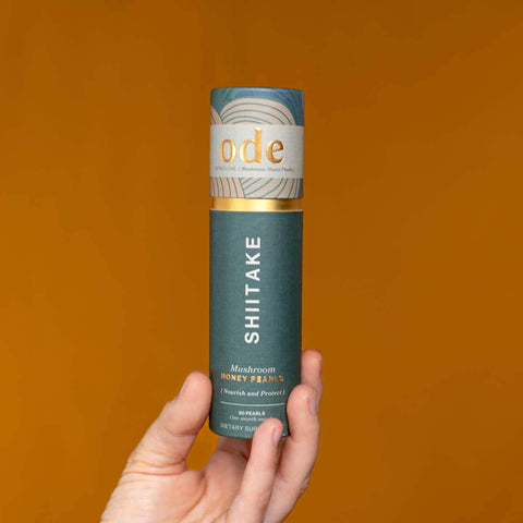 Hand holding tube of Shiitake Mushroom Honey Pearls against an orange background. 