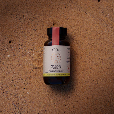 Jar of Ora Adrenal Tonic+ 60 capsules placed on sand. Vegan supplement that relieves symptoms of stress, mild anxiety, and fatigue.
