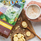 Power Super Foods Cacao Butter Buttons lifestyle shot of the pouch beside a bowl of white buttons and a hand holding a mug, styled lifestyle photo