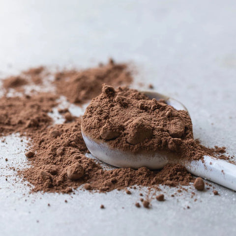 Power Super Foods Cacao Powder lifestyle shot of loose cacao powder heaped on a white spoon on a grey surface, styled lifestyle photo