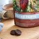 Power Super Foods Ceremonial Cacao Paste Raw Buttons lifestyle shot of the pouch labelled Cacao Paste beside two dark discs and a mug