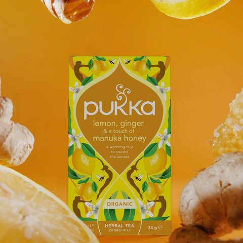 Pukka lemon, ginger, and manuka honey tea box on an orange background with lemons and ginger.