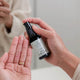 Person holding a bottle of 'arcturus' skincare product with another hand open palm up.
