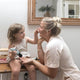 Woman applying makeup to a child's hand in a home setting.