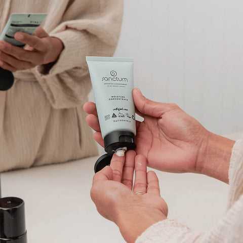 Person applying Sanctum moisturizing cream to their hand with a neutral background.