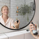 Person applying makeup in front of a mirror with a plant in the background.
