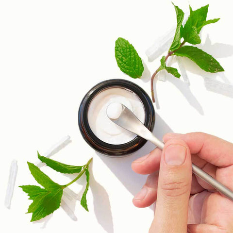Hand scooping Solid Toothpaste Fresh Mint with Fluoride from a jar, surrounded by mint on a white background