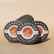 Three tins of SunButter tinted sunscreen on a beige background with a rock.