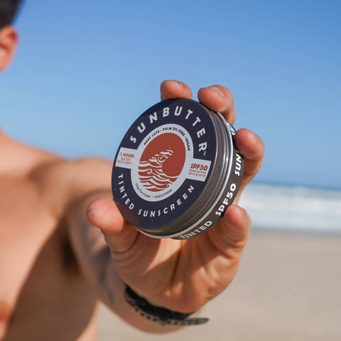 Person holding a SunButter sunscreen container on a beach