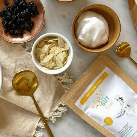 Assorted food items including dried fruits, yogurt, and a pack of supercharged food golden gut powder on a marble surface.
