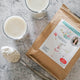 Flat lay of a 100g packet of Supercharged Food Love Your Gut Powder, a spoonful of white powder, and a glass of water with the powder mixed in.