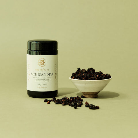 Supplement bottle labeled 'Superfeast Schisandra' with a bowl of schisandra berries on a light green background