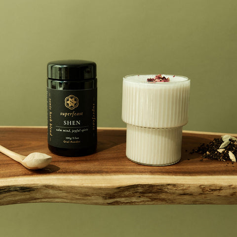 Superfeast Shen supplement bottle on a wooden surface with a white glass and spoon.