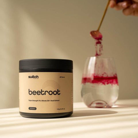 Container of 'switch' beetroot powder with a glass of pink liquid on a neutral background.