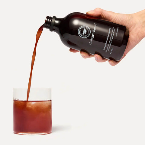 The Beauty Chef Collagen Boost 500ml lifestyle shot of a hand pouring the dark liquid from the bottle into a glass over ice, close up