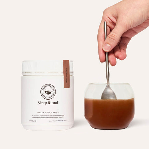 Sleep Ritual container next to a glass of the chocolate oral powder being mixed in with a spoon. Set against white background. 
