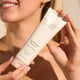 The Jojoba Company Jojoba Bead Cleanser 125ml lifestyle close up of a woman holding the tube near her chin, face partly shown, golden light