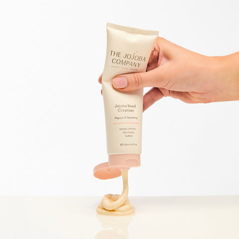 The Jojoba Company Jojoba Bead Cleanser 125ml lifestyle shot of a hand squeezing the tube, with cleanser dispensed onto a white surface below it