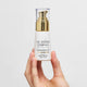 Hand holding a bottle of The Jojoba Company Pigmentation Oil against a light gray background.