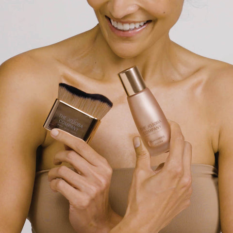 Model holding The Jojoba Company Illuminating Jojoba and kabuki brush.