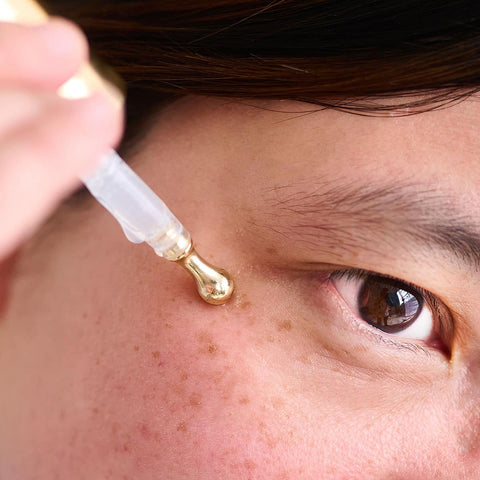 Person applying a dropper of skincare product to their face.