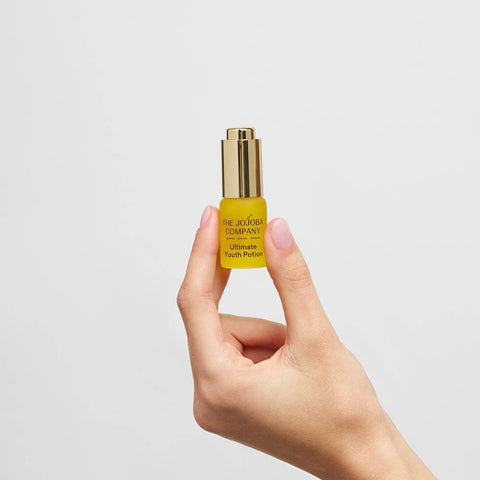Hand holding a yellow skincare bottle with gold cap against a light gray background.