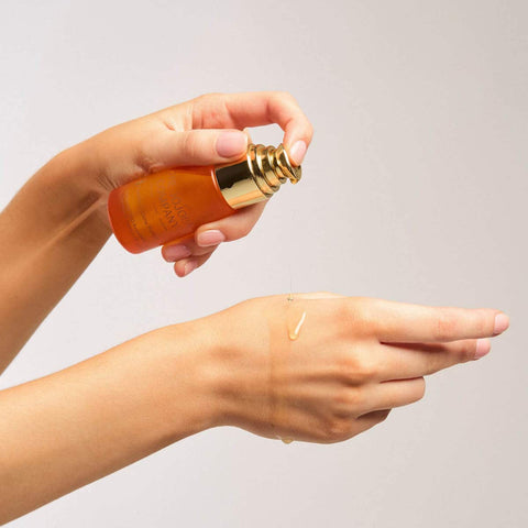 The Jojoba Company Vitamin C Glow Potion Kit lifestyle shot of a hand holding the gold topped bottle over a wrist with serum on the skin