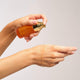 The Jojoba Company Vitamin C Glow Potion Kit lifestyle shot of a hand holding the gold topped bottle over a wrist with serum on the skin