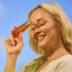 The Jojoba Company Vitamin C Glow Potion Kit lifestyle shot of a smiling woman with blonde hair holding an amber dropper bottle to her forehead