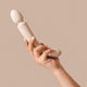 Hand holding The Natural Love Company Cassia, a dual-ended marvel with a deeply rumbly wand vibrator on one end paired with a G-spot targeting dildo on the other, all encased in buttery soft pastel pink silicone.